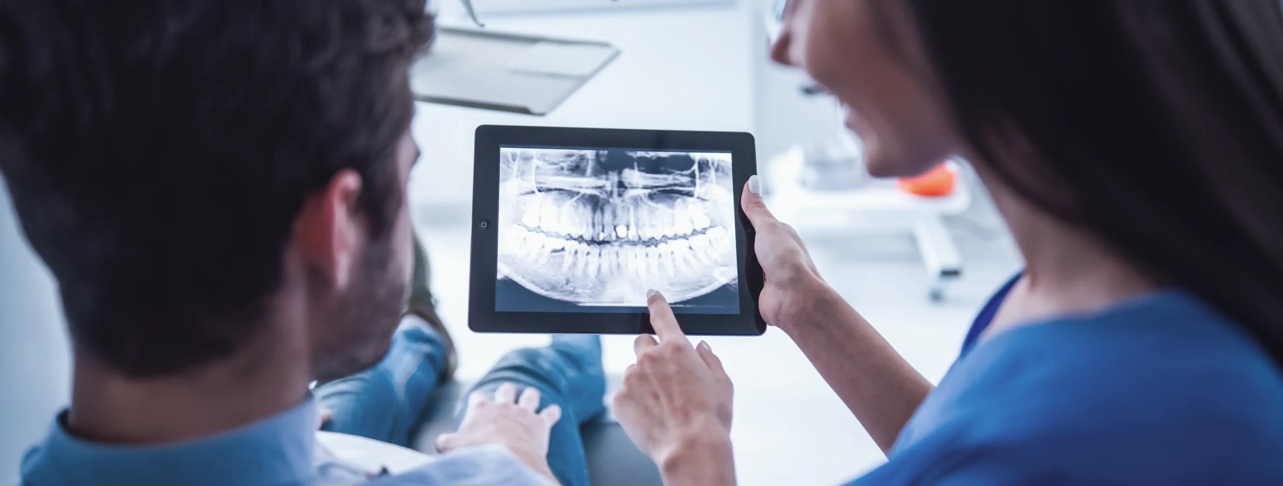 Dentist and patient reviewing a panoramic jaw X-ray displayed on a tablet in a dental clinic