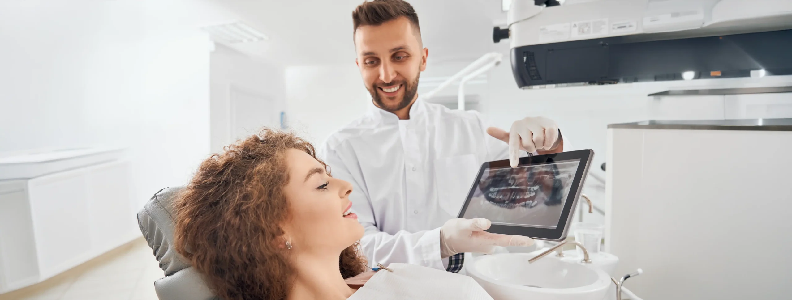 Dentist showing a smiling patient their dental X-ray images on a tablet during chairside consultation