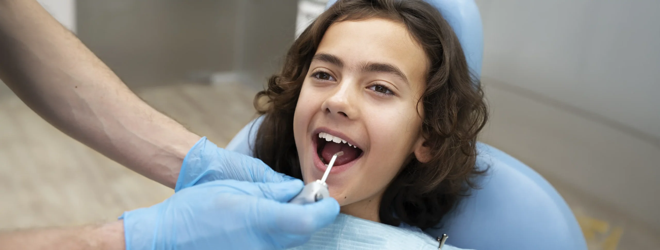 Young girl smiling in a dental chair while a dentist uses a handpiece near her open mouth