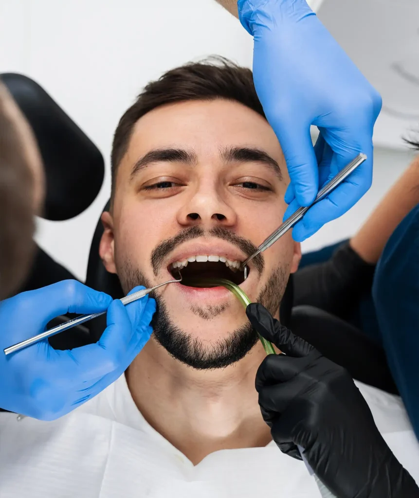 Male patient in dental chair with mouth open while two dental professionals work with instruments during a gum examination