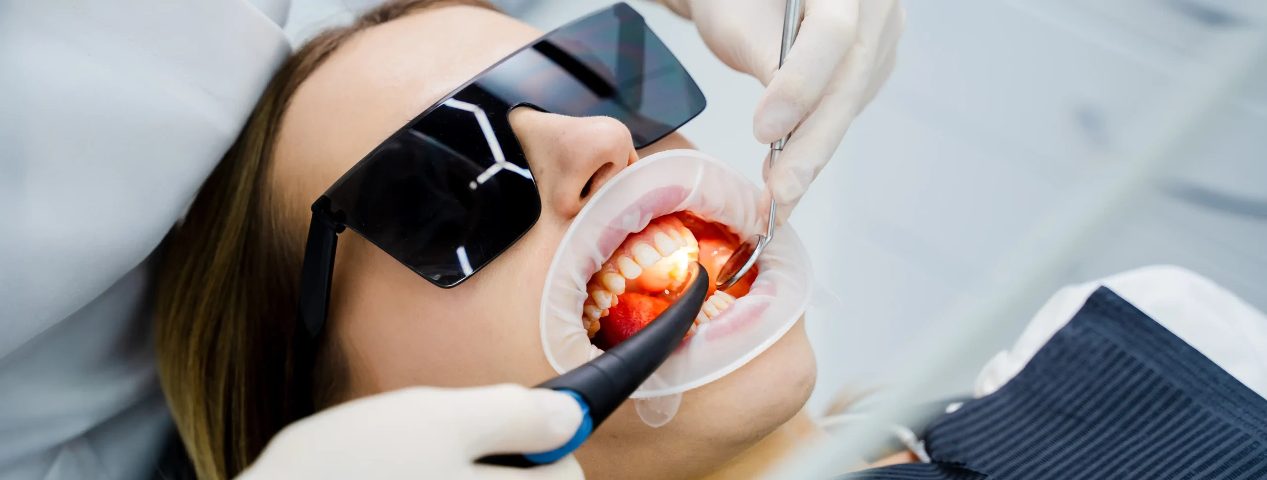 Patient wearing protective glasses during a gum treatment procedure with a light-curing device and dental mirror