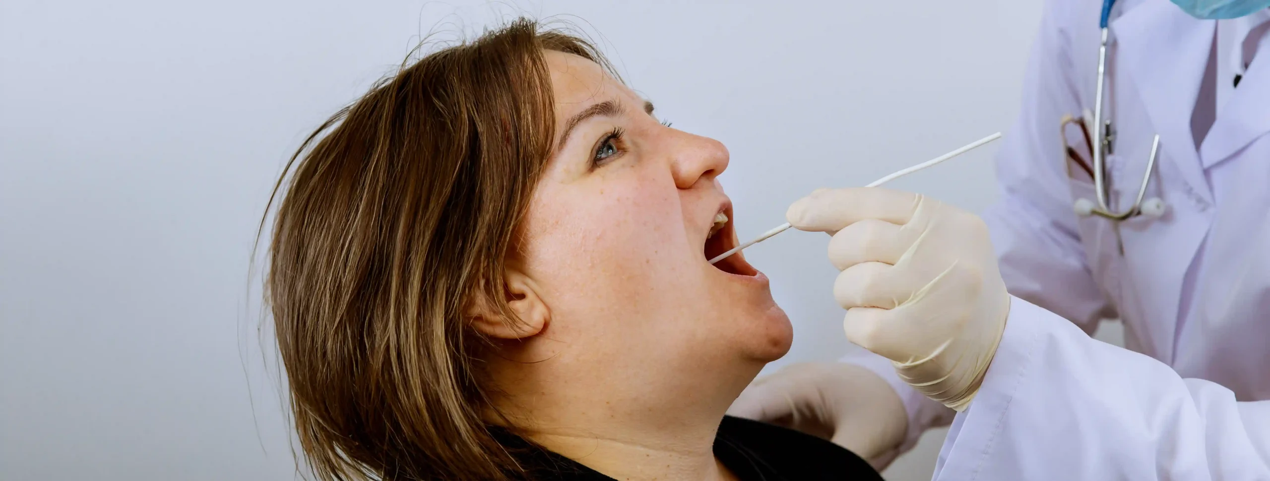 Healthcare professional using a swab to collect a sample from inside a patient's open mouth