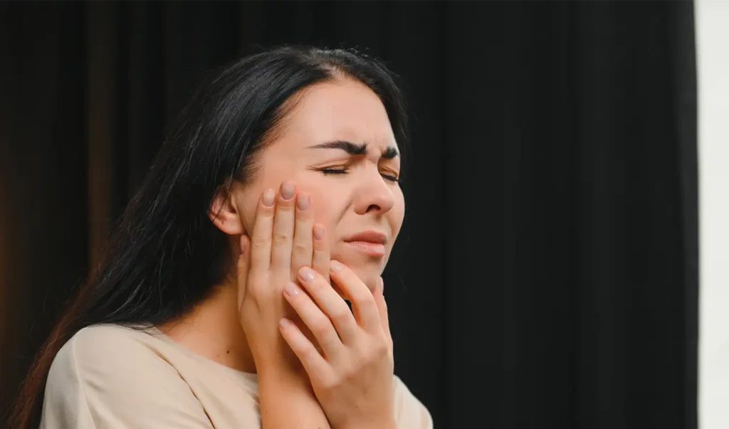 A woman holding her cheek in pain due to a severe dental toothache.