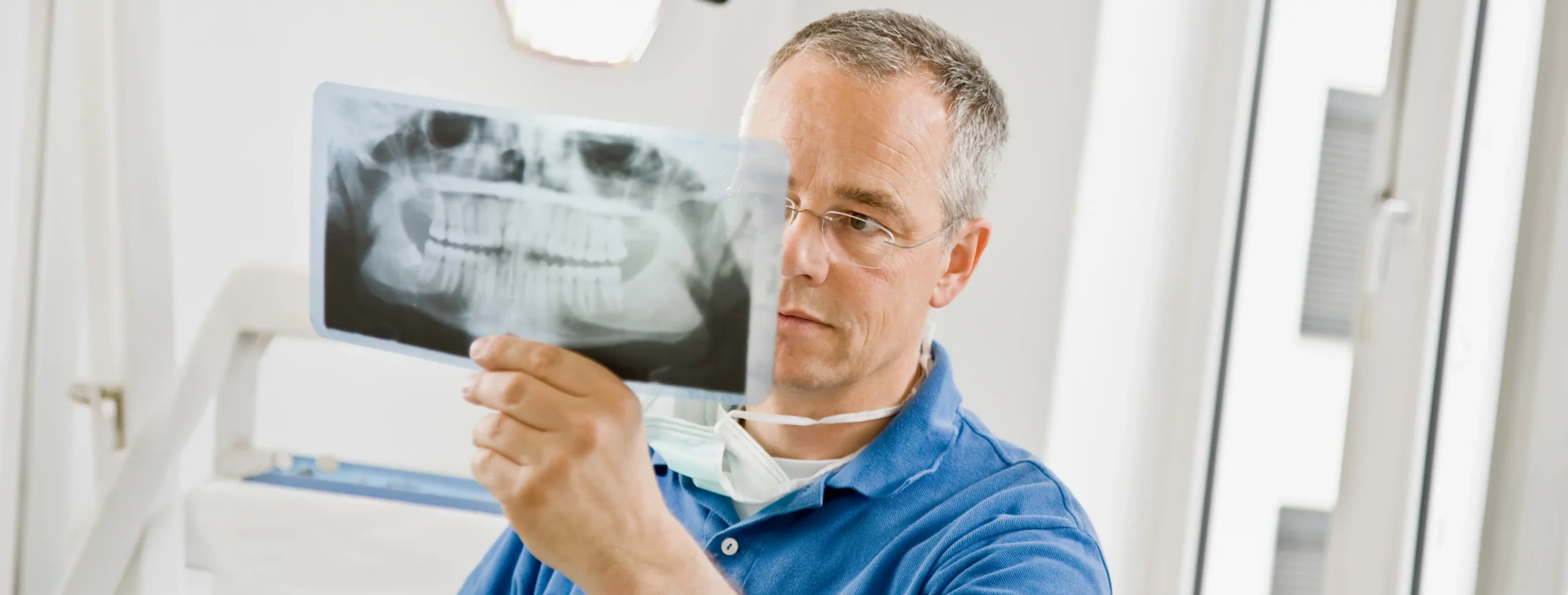 Dentist in a clinic examining a panoramic OPG X-ray film held up to the light