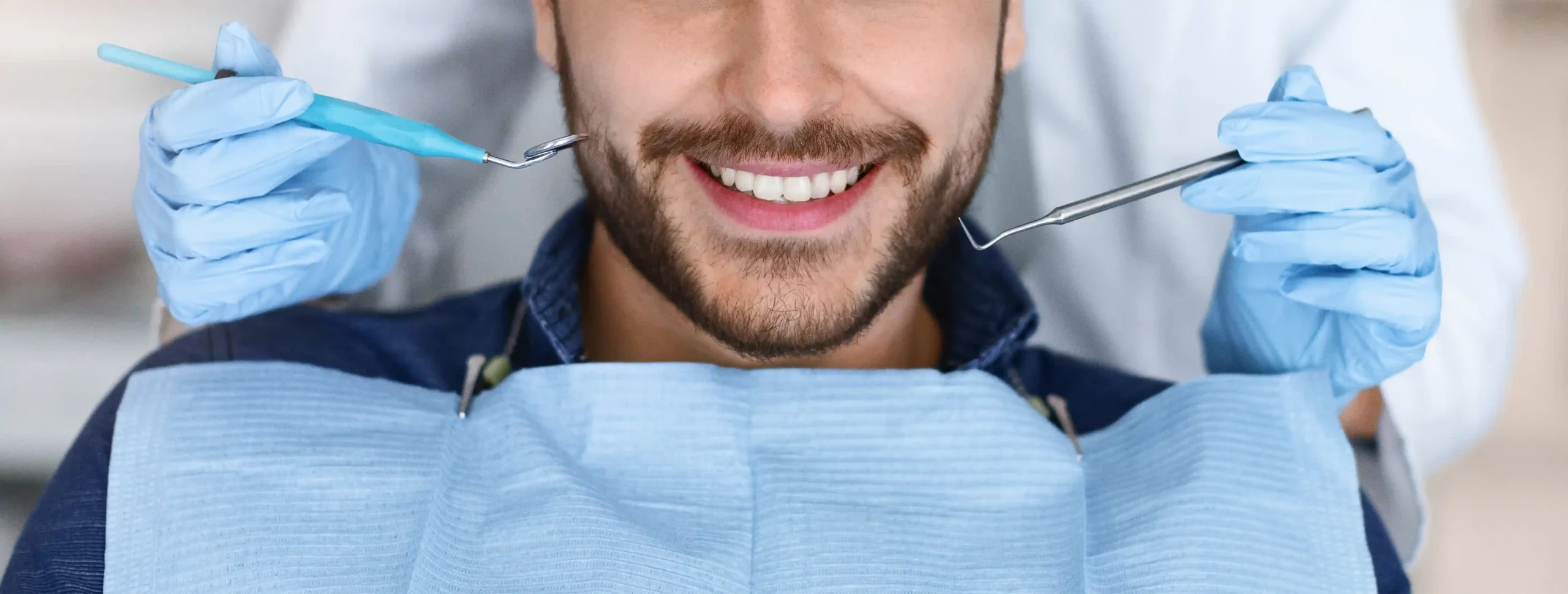 Male patient in dental chair smiling while a dentist's gloved hands hold a composite applicator and dental explorer