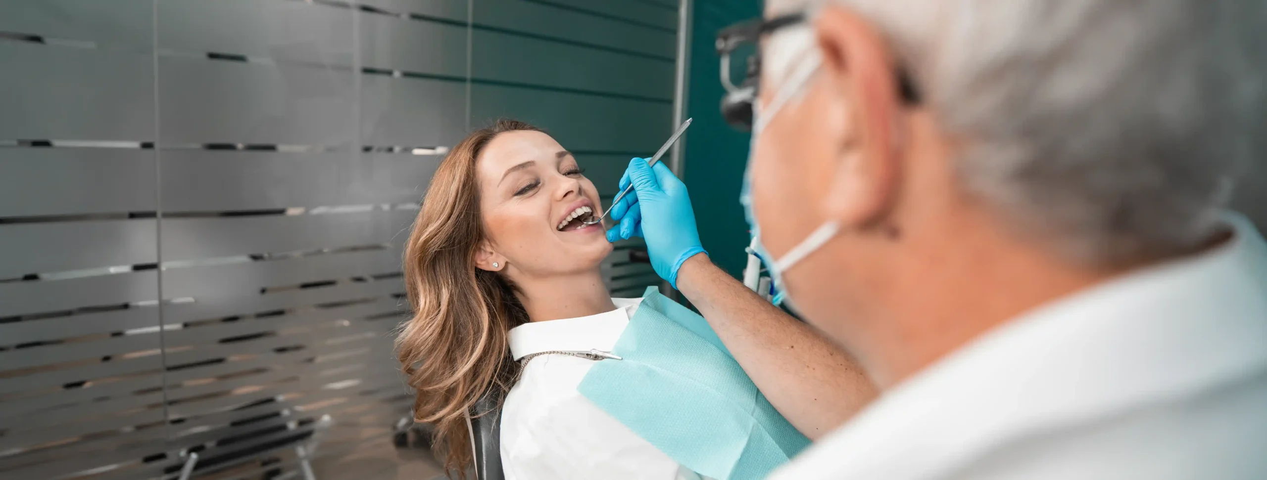 Older male dentist using a dental instrument to examine a female patient's teeth during a check-up