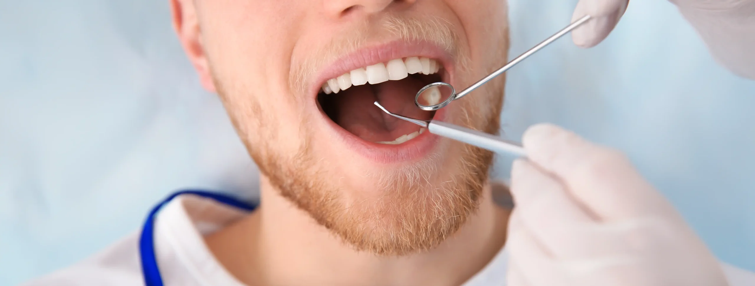 Male patient with mouth open while a gloved dentist uses a dental mirror and explorer during an examination