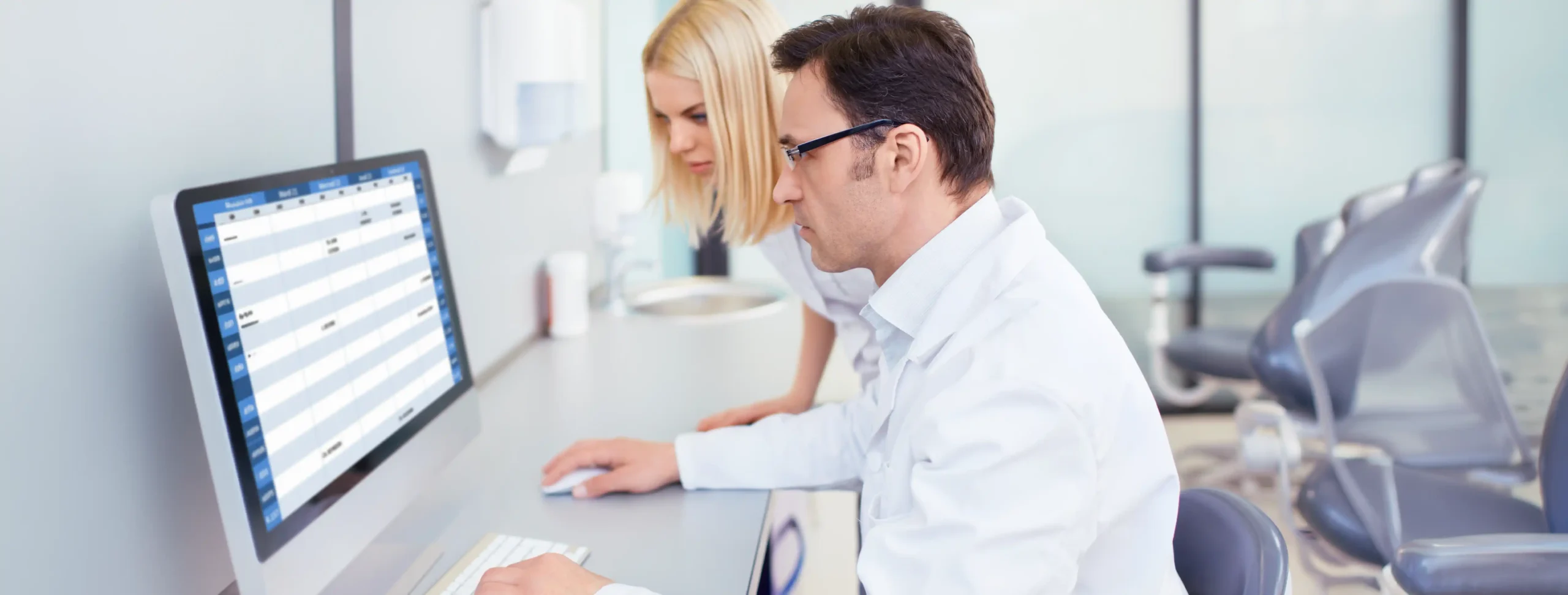 Two dental clinic staff members reviewing patient scheduling software on a computer at the front desk