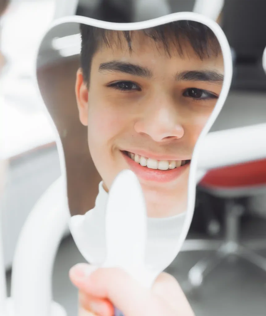 Young man smiling at his reflection through a tooth-shaped frame after a smile assessment at the dental clinic