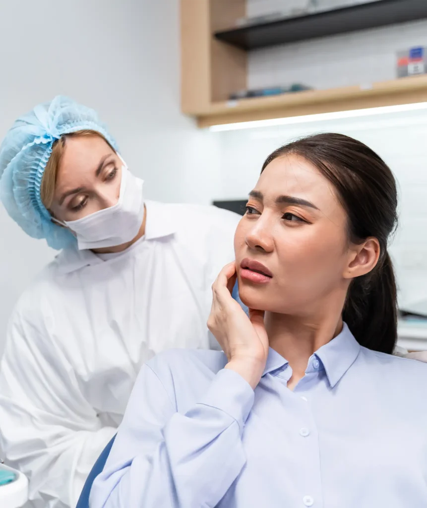 Female patient holding her jaw in pain while a masked dentist looks on during a tooth pain assessment