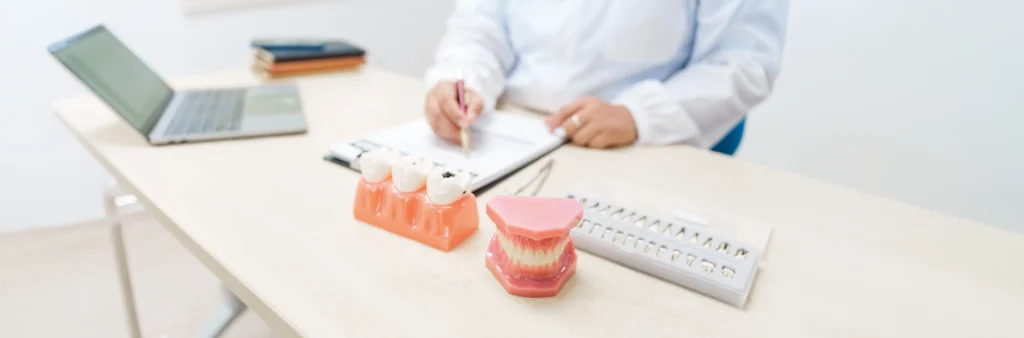 Dentist consulting on implant supported dentures with dental models on desk.