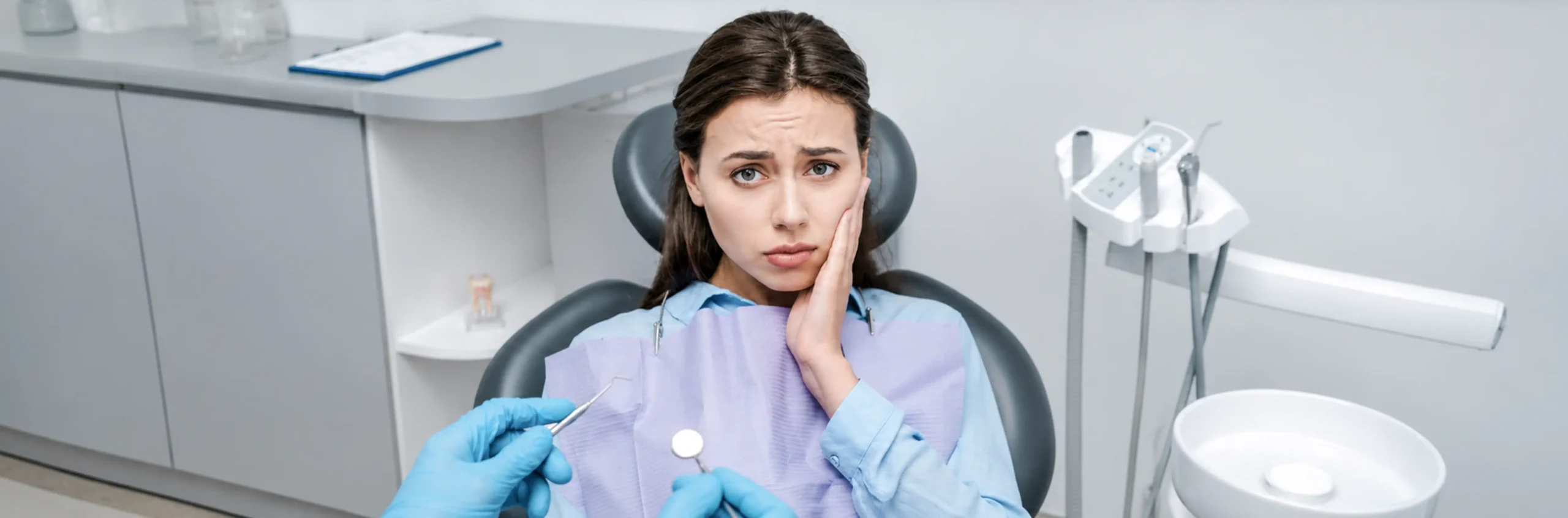 Woman wincing in pain, holding jaw during dental appointment