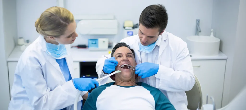 Dentist and assistant performing wisdom tooth removal on patient in dental chair