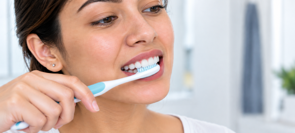 Woman gently brushing her front teeth with a soft-bristled toothbrush at the gum line