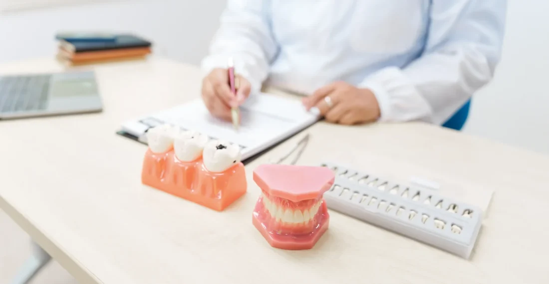 Dentist consulting on implant supported dentures with dental models on desk.
