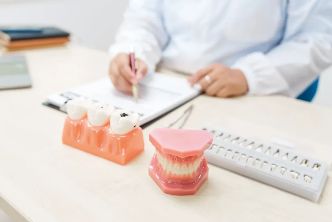 Dentist consulting on implant supported dentures with dental models on desk.