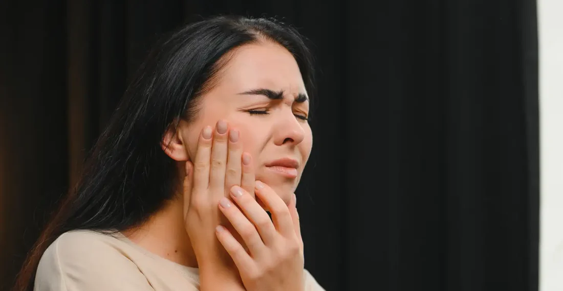 A woman holding her cheek in pain due to a severe dental toothache.
