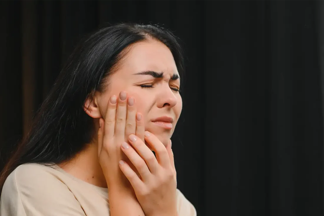 A woman holding her cheek in pain due to a severe dental toothache.