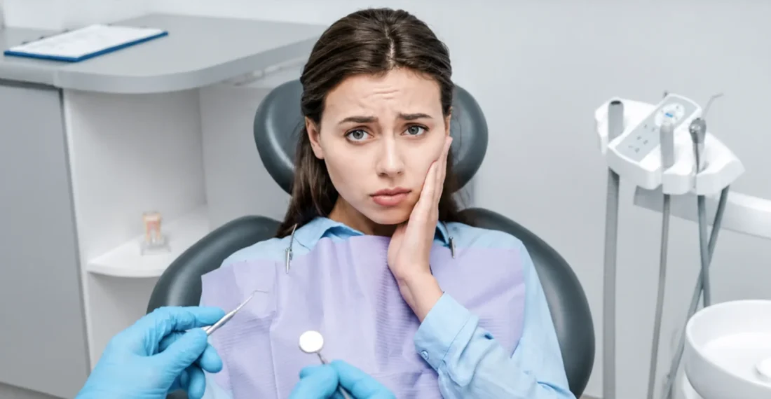 Woman wincing in pain, holding jaw during dental appointment