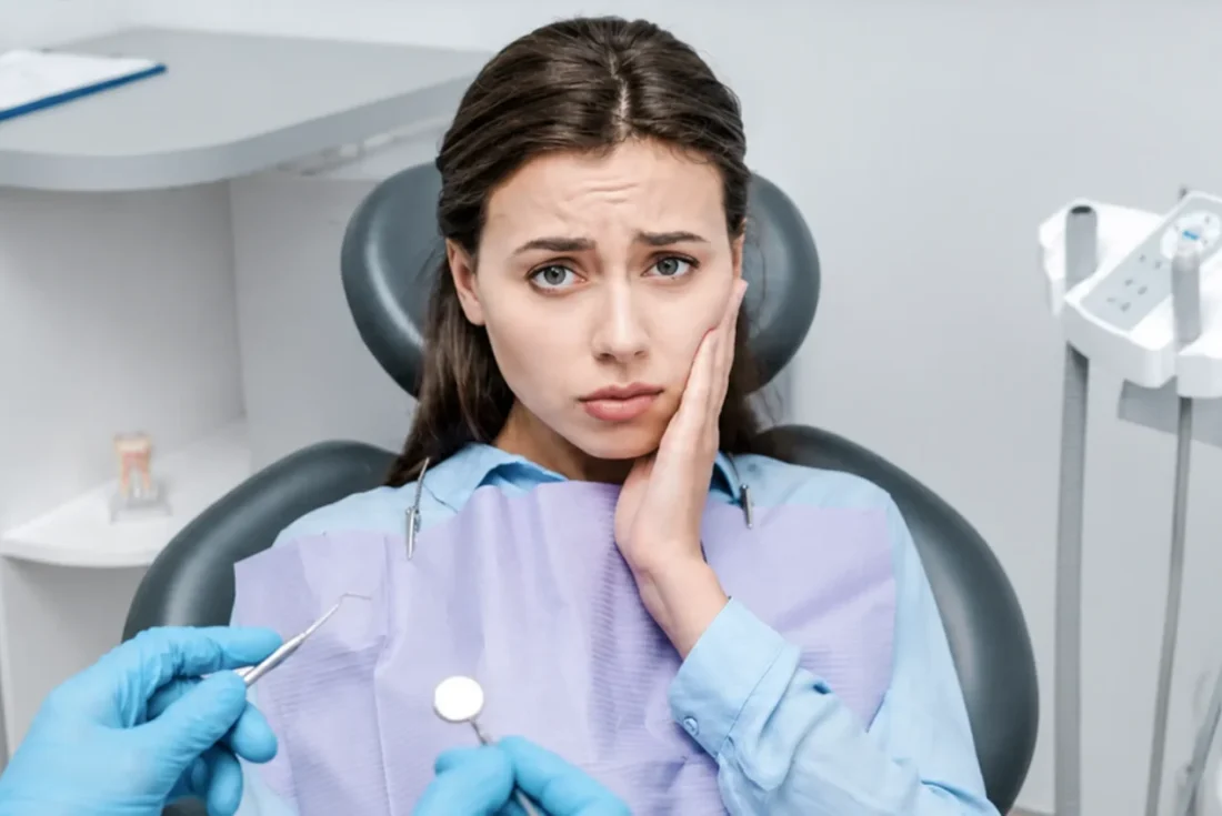 Woman wincing in pain, holding jaw during dental appointment