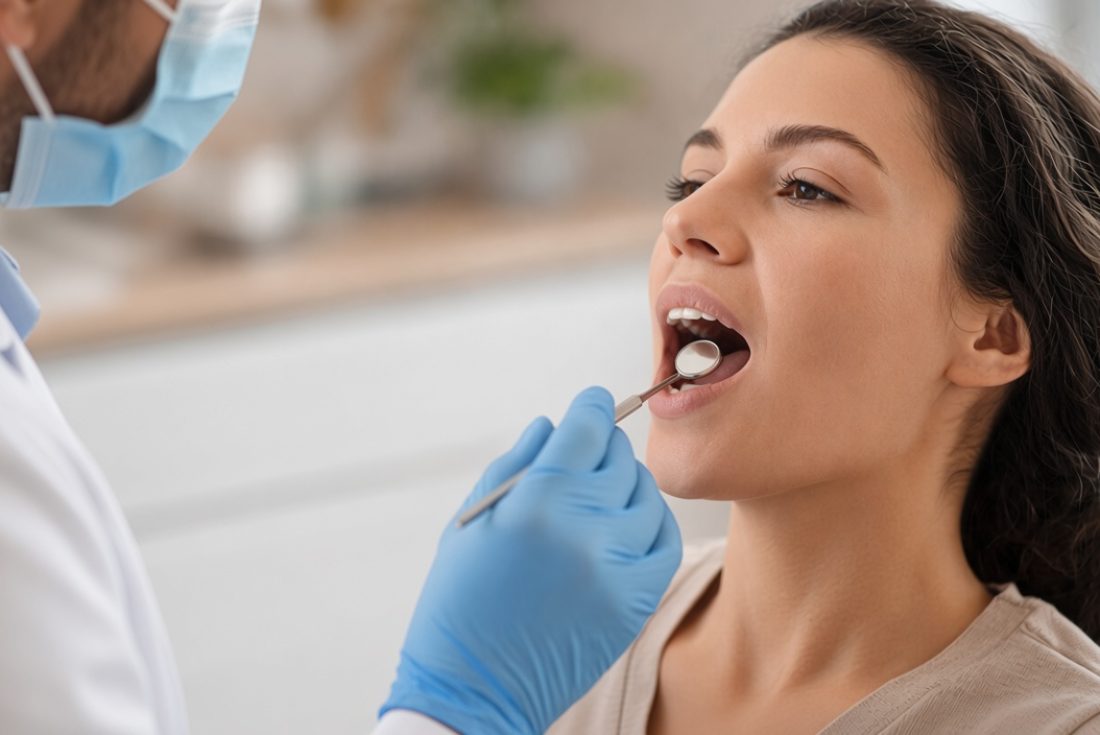 Dentist in mask and gloves examining a smiling patient's teeth with a dental mirror